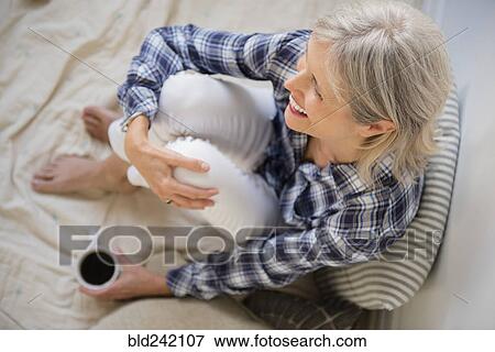 Stock Photo - Caucasian woman sitting on bed drinking coffee. Fotosearch