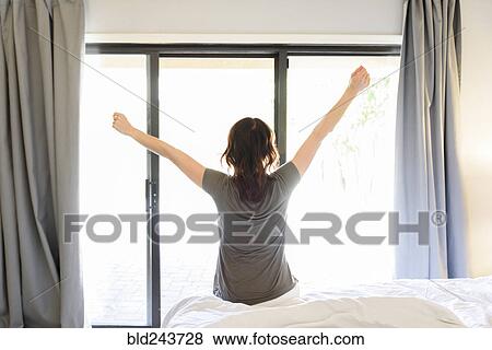 Stock Photo - Caucasian woman sitting on bed stretching arms. Fotosearch