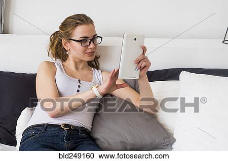 Stock Image - Caucasian woman sitting on bed using digital tablet. Fotosearch