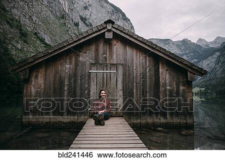 Stock Photograph - Caucasian woman sitting on dock at remote cabin. Fotosearch
