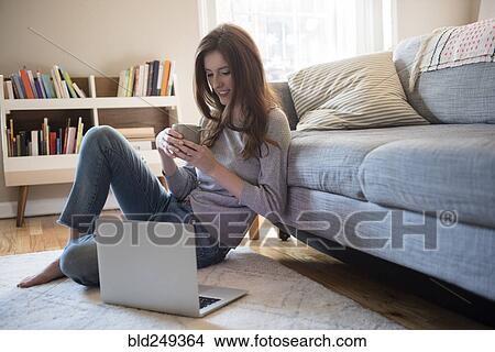 Picture - Caucasian woman sitting on floor with coffee and laptop. Fotosearch
