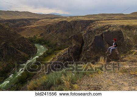 Caucasian woman sitting on mountain rocks photographing river View Large Photo Image Stock Photograph - Caucasian woman sitting on mountain rocks photographing river. Fotosearch