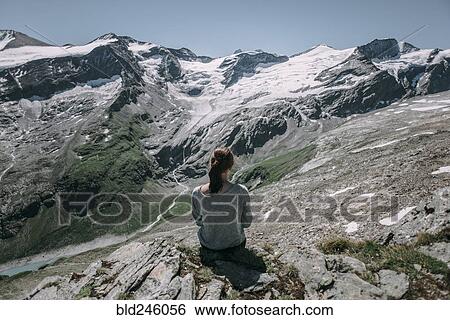 Stock Photograph - Caucasian woman sitting on rock admiring scenic view of mountain. Fotosearch