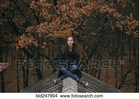 Picture - Caucasian woman sitting on roof in autumn. Fotosearch