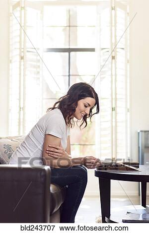 Caucasian woman sitting on sofa reading magazine View Large Photo Image Stock Photo - Caucasian woman sitting on sofa reading magazine. Fotosearch