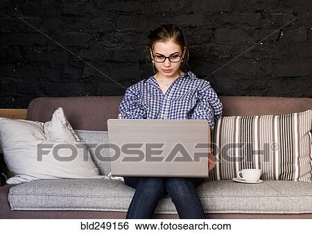 Stock Photograph - Caucasian woman sitting on sofa using laptop. Fotosearch
