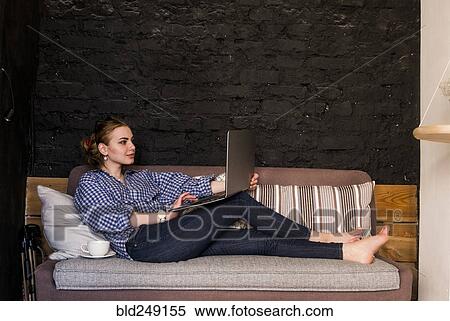 Stock Photography - Caucasian woman sitting on sofa using laptop. Fotosearch