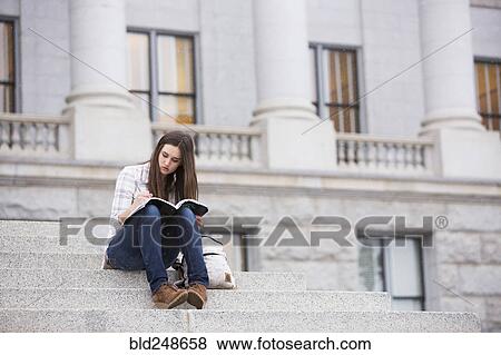 Stock Photo - Caucasian woman sitting on staircase writing in notebook. Fotosearch