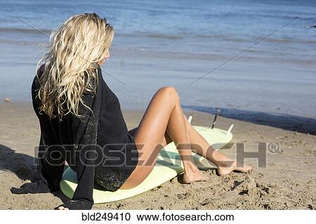 Stock Image - Caucasian woman sitting on surfboard on beach. Fotosearch