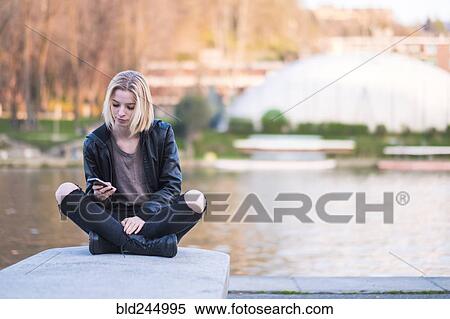Caucasian woman sitting on wall near river texting on cell phone View Large Photo Image Stock Photography - Caucasian woman sitting on wall near river texting on cell phone. Fotosearch