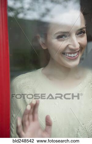 Stock Image - Caucasian woman smiling behind foggy window. Fotosearch