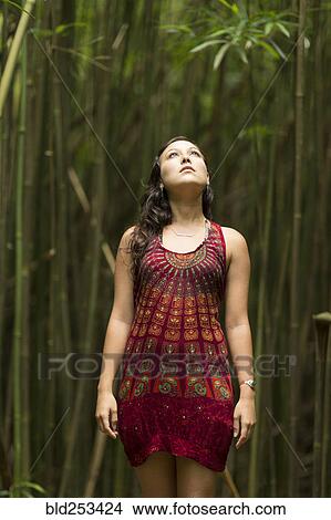 Picture - Caucasian woman standing in bamboo forest and looking up. Fotosearch