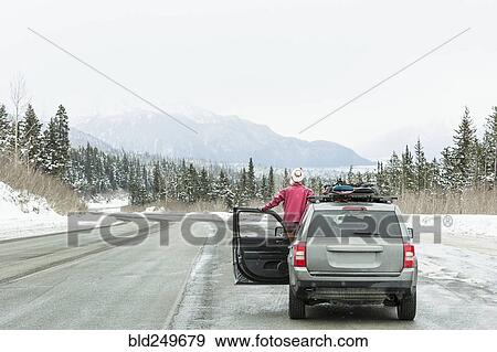 Stock Photo - Caucasian woman standing in car in winter admiring scenic view. Fotosearch