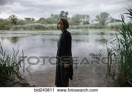 Stock Image - Caucasian woman standing near river in rain. Fotosearch