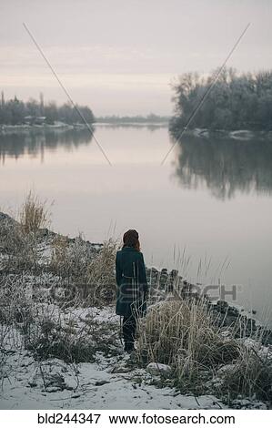 Stock Photo - Caucasian woman standing near river in winter. Fotosearch