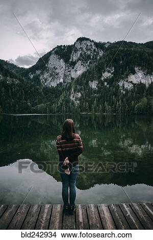 Picture - Caucasian woman standing on dock admiring scenic view of mountain. Fotosearch