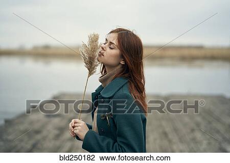 Caucasian woman standing on dock smelling stalk of grass View Large Photo Image Stock Image - Caucasian woman standing on dock smelling stalk of grass. Fotosearch