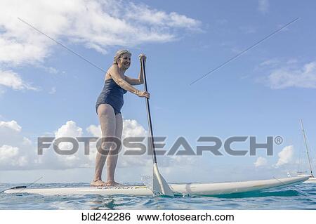 Stock Photograph - Caucasian woman standing on paddle board on ocean. Fotosearch