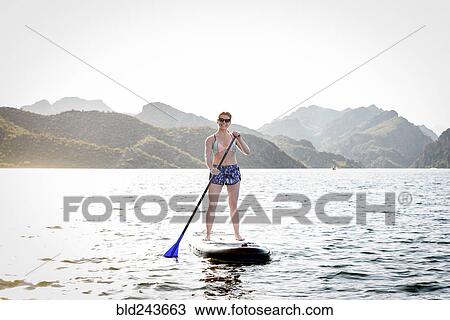 Stock Image - Caucasian woman standing on paddleboard in river. Fotosearch