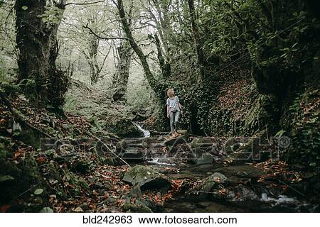 Stock Image - Caucasian woman standing on rock near forest stream. Fotosearch