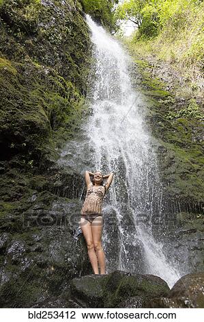 Stock Image - Caucasian woman standing on rock near waterfall. Fotosearch