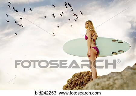 Caucasian woman standing on rock holding surfboard View Large Photo Image Stock Image - Caucasian woman standing on rock holding surfboard. Fotosearch