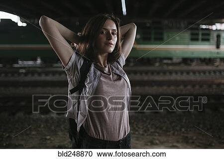 Stock Image - Caucasian woman stretching arms near train tracks at night. Fotosearch