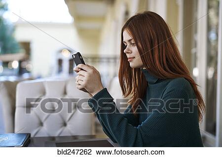 Stock Image - Caucasian woman texting on cell phone at restaurant. Fotosearch