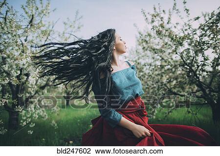 Stock Image - Caucasian woman tossing hair near flowering trees. Fotosearch