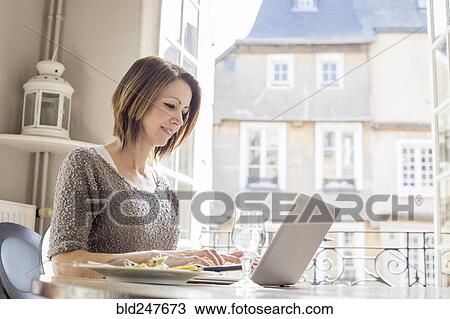 Caucasian woman typing on laptop and eating meal View Large Photo Image Stock Image - Caucasian woman typing on laptop and eating meal. Fotosearch