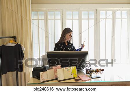 Stock Photograph - Caucasian woman using computer in clothing store. Fotosearch