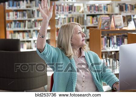 Stock Photograph - Caucasian woman using computer in library raising hand. Fotosearch