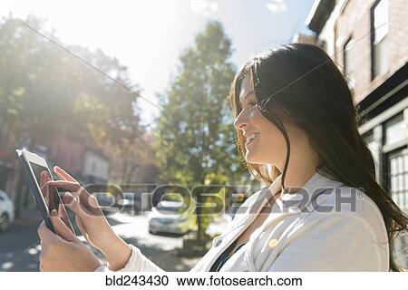 Stock Image - Caucasian woman using digital tablet in city. Fotosearch