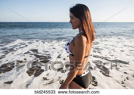 Stock Image - Caucasian woman wading in ocean waves on beach. Fotosearch