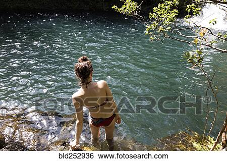 Stock Photograph - Caucasian woman wading in pool near waterfall. Fotosearch