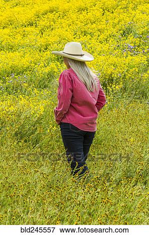 Stock Photo - Caucasian woman walking in field of yellow flowers. Fotosearch