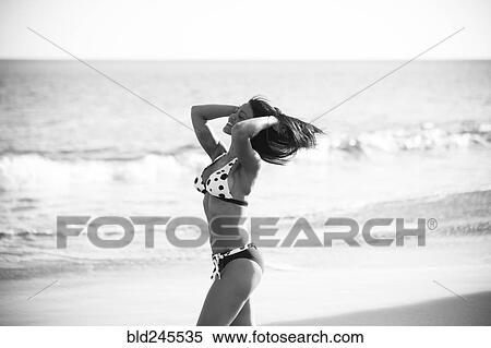 Stock Photography - Caucasian woman walking on beach with hands in hair. Fotosearch