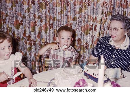 Stock Photo - Caucasian woman watching grandson and granddaughter eating cake. Fotosearch