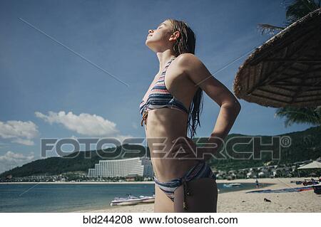 Stock Photo - Caucasian woman wearing bikini enjoying sunlight at beach. Fotosearch