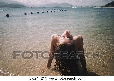 Stock Image - Caucasian woman wearing bikini sitting in waves on beach. Fotosearch