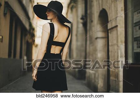 Stock Photo - Caucasian woman wearing black dress and sun hat in street. Fotosearch