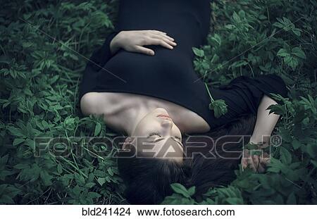 Picture - Caucasian woman wearing dress laying in green foliage. Fotosearch