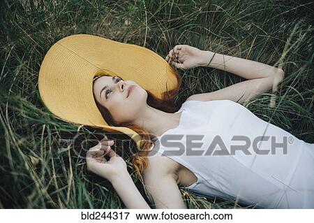 Stock Photo - Caucasian woman wearing hat laying in grass. Fotosearch