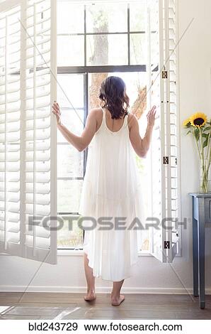 Caucasian woman wearing nightgown opening window shutters View Large Photo Image Stock Photo - Caucasian woman wearing nightgown opening window shutters. Fotosearch