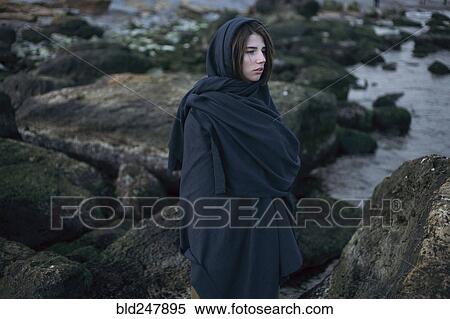 Stock Photography - Caucasian woman wearing scarf on rocks at ocean. Fotosearch