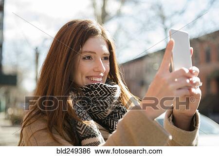 Stock Photograph - Caucasian woman wearing scarf posing for cell phone selfie. Fotosearch