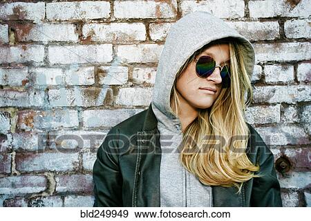 Stock Photo - Caucasian woman wearing sunglasses near brick wall. Fotosearch