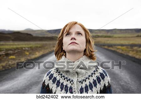 Stock Image - Caucasian woman wearing sweater in road looking up. Fotosearch