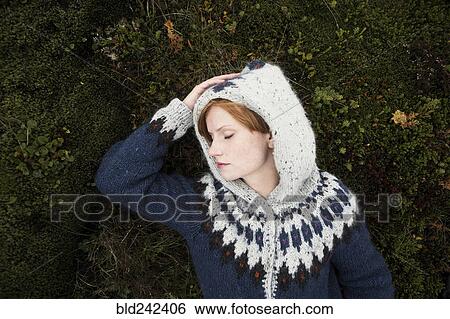 Stock Photograph - Caucasian woman wearing sweater laying on moss. Fotosearch