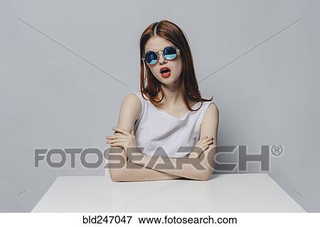 Stock Photo - Caucasian woman with attitude sitting at table wearing sunglasses. Fotosearch